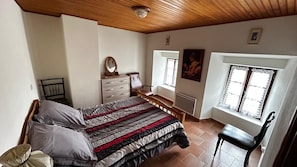 Ein Schlafzimmer mit Bett, Kommode, Stuhl und Fenstern.