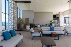 A spacious lounge area with sofas, armchairs, and a coffee table, featuring large windows and a city view. - 1 Bedroom w/ Captivating Ocean View Costa del Este (Panamá)