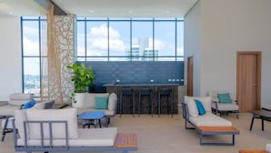 A modern lounge area with seating, a bar, and large windows offering a city view. - Coastal View Executive Studio in Panama (Panamá)