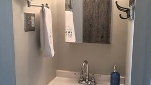 Un baño con un lavamanos blanco, un espejo, un perchero para toallas y un dispensador de jabón azul.
