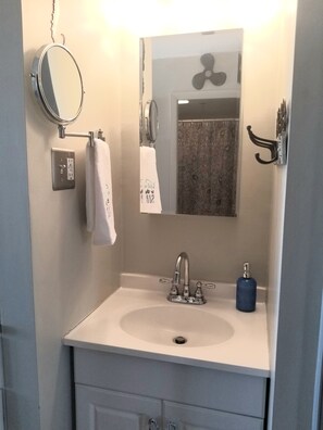 A bathroom with a white sink, a mirror, a towel rack, and a blue soap dispenser. - Oceanfront 1-bedroom condo on North Beach with a pool! (Hampton)