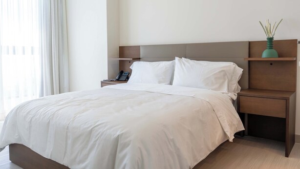 A hotel room with a large bed, a bedside table with a phone, and a nightstand with a vase. - Serviced 2 bedroom with Ocean Views in Costa del Este (Panamá)