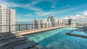 A rooftop infinity pool with lounge chairs, a city skyline view, and a clear sky. - Serviced 2 bedroom with Ocean Views in Costa del Este (Panamá)