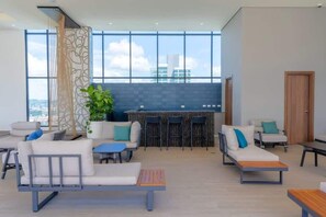 A modern lounge area with seating, a bar, and large windows offering city views. - Elegant Studio Overlooking Costa del Este Park (Panamá)