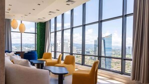 A modern lounge with large windows, a green wall, and a city view.