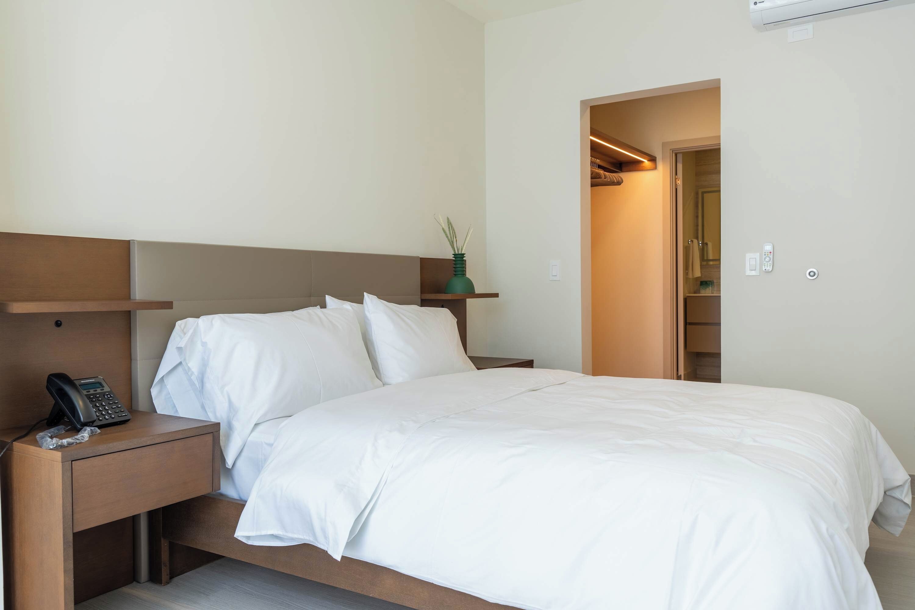 Een hotelkamer met een bed, nachtkastje, telefoon en een kleine plant.