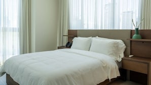 Ein Hotelzimmer mit einem Bett, einem Nachttisch, einem Telefon und Blick auf Gebäude durch leichte Vorhänge.