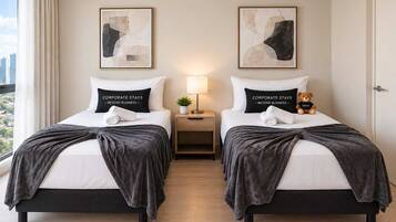 A hotel room with two beds, each with a pillow stating 'CORPORATE STAYS - BEYOND BUSINESS,' a nightstand with a lamp, and a teddy bear on one bed.
