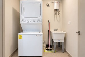 A compact laundry room with a front-loading washer and dryer, a sink, and a water heater. - Costa del Este 2-Bedroom Corporate Rental | 2 Baths, Water Views & Pool (Panamá)