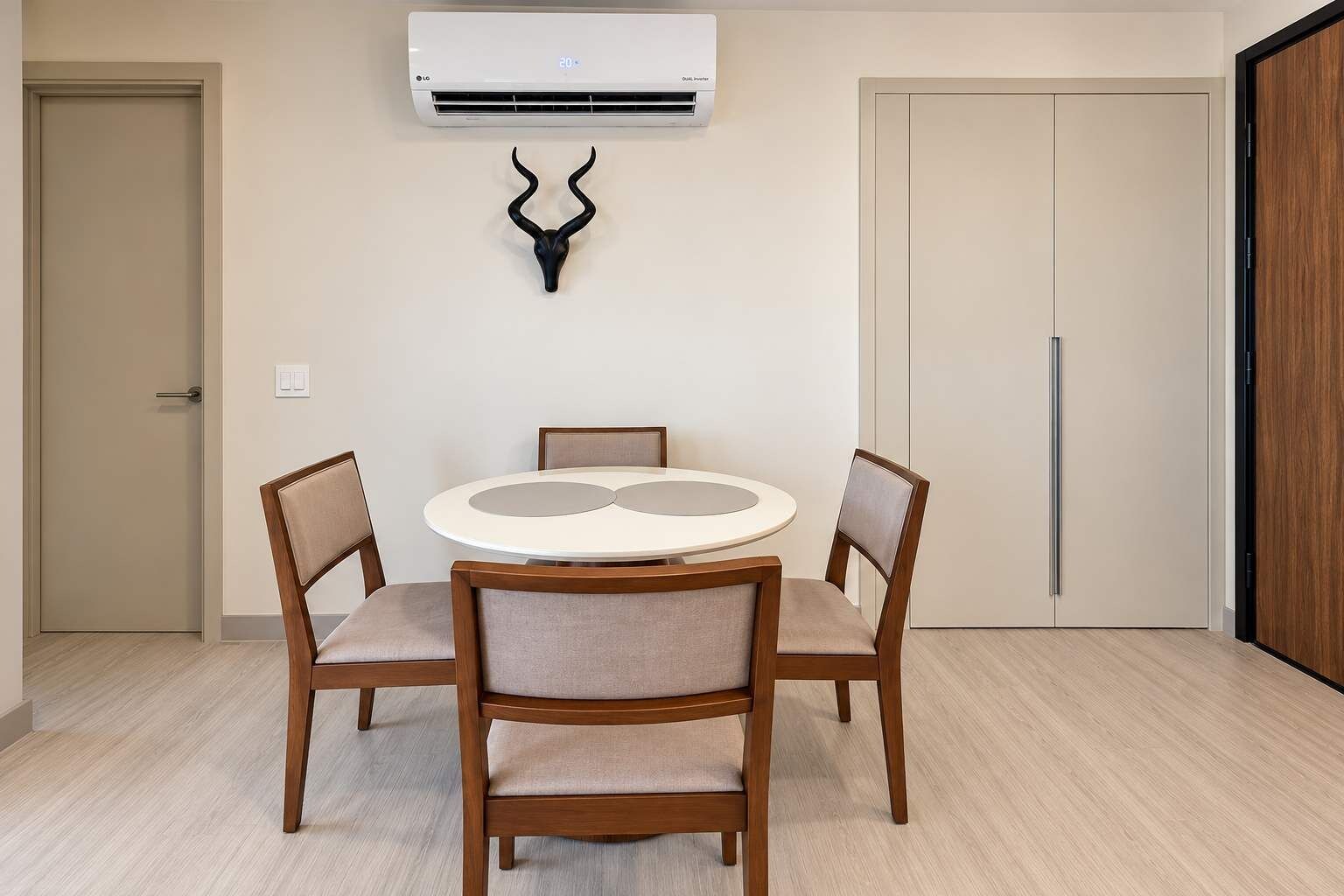 Een eetruimte met een ronde tafel en vier stoelen, een airconditioning en een houten deur.