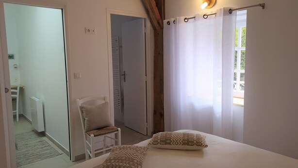 Een slaapkamer met een bed, twee kussens, een stoel, een radiator en een raam met gordijnen.