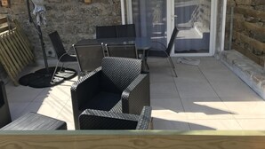 Een terras met buitenmeubilair, een tafel, stoelen, een schuifdeur en een stenen muur.