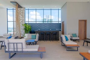 Eine moderne Lounge mit Sitzgelegenheiten, einer Bar und großen Fenstern mit Blick auf die Stadt.