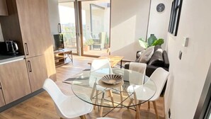 A modern kitchen with a glass dining table, white chairs, and a black sofa in the living area. - Furnished 1 Bedroom in Santiago in Somma Asturias (Las Condes)