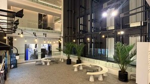 A spacious indoor area with multiple levels, a central seating area with round tables, and potted plants. - Furnished 1 Bedroom in Santiago in Somma Asturias (Las Condes)