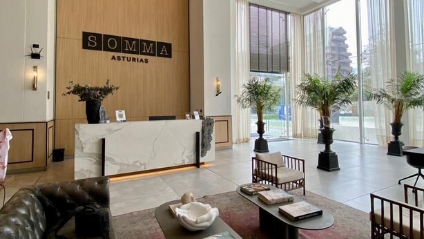 A modern hotel lobby with a reception desk, leather seating, large windows, and potted plants. - Furnished 1 Bedroom in Santiago in Somma Asturias (Las Condes)