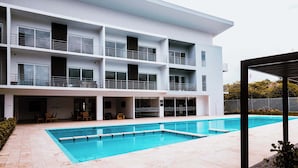 Un bâtiment moderne doté d’une piscine, de nombreux balcons et d’un espace extérieur aménagé pour s’asseoir.