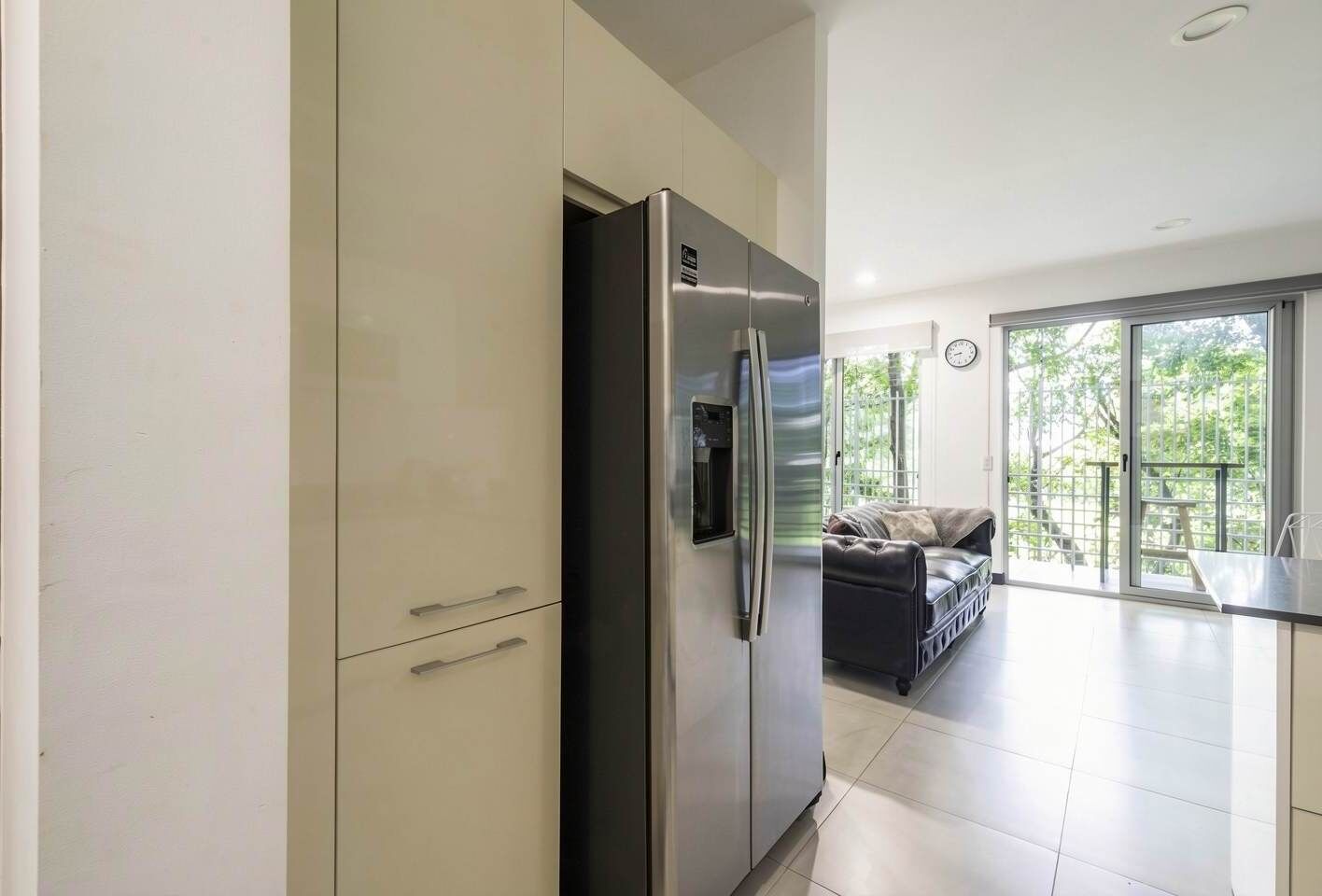 A modern kitchen with a built-in refrigerator, a dining area with a table and chairs, and a view of the outdoors through large windows.
