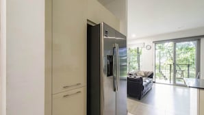 Une cuisine moderne dotée d’un réfrigérateur encastré, d’un coin repas avec une table et des chaises, et offrant une vue sur l’extérieur grâce à de grandes fenêtres.