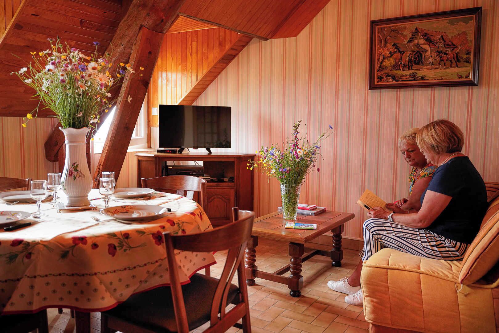 Ein Essbereich mit Holztisch, Stühlen, einem Blumenstrauß, einem Fernseher und einem Gemälde an der Wand.