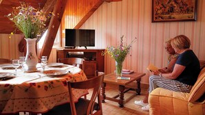 Ein Essbereich mit Holztisch, Stühlen, einem Blumenstrauß, einem Fernseher und einem Gemälde an der Wand.