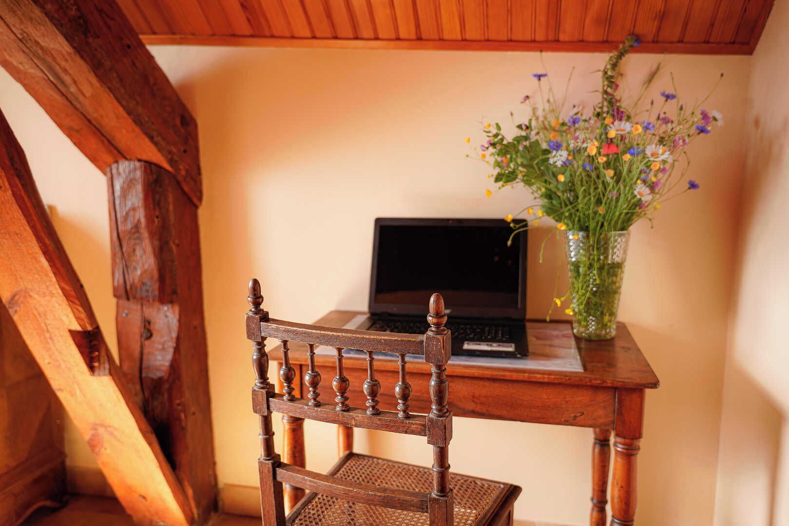 A wooden chair and desk with a laptop and a vase of flowers.