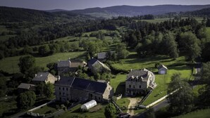 Eine Vogelperspektive auf ein ländliches Dorf mit Steinhäusern, einem zentralen Haus mit einer markanten Treppe und umgebender Vegetation.
