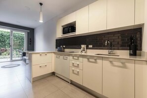 A modern kitchen with white cabinets, a black backsplash, and a built-in microwave. - Furnished 1 Bedroom Apartment in San José (Pozos)