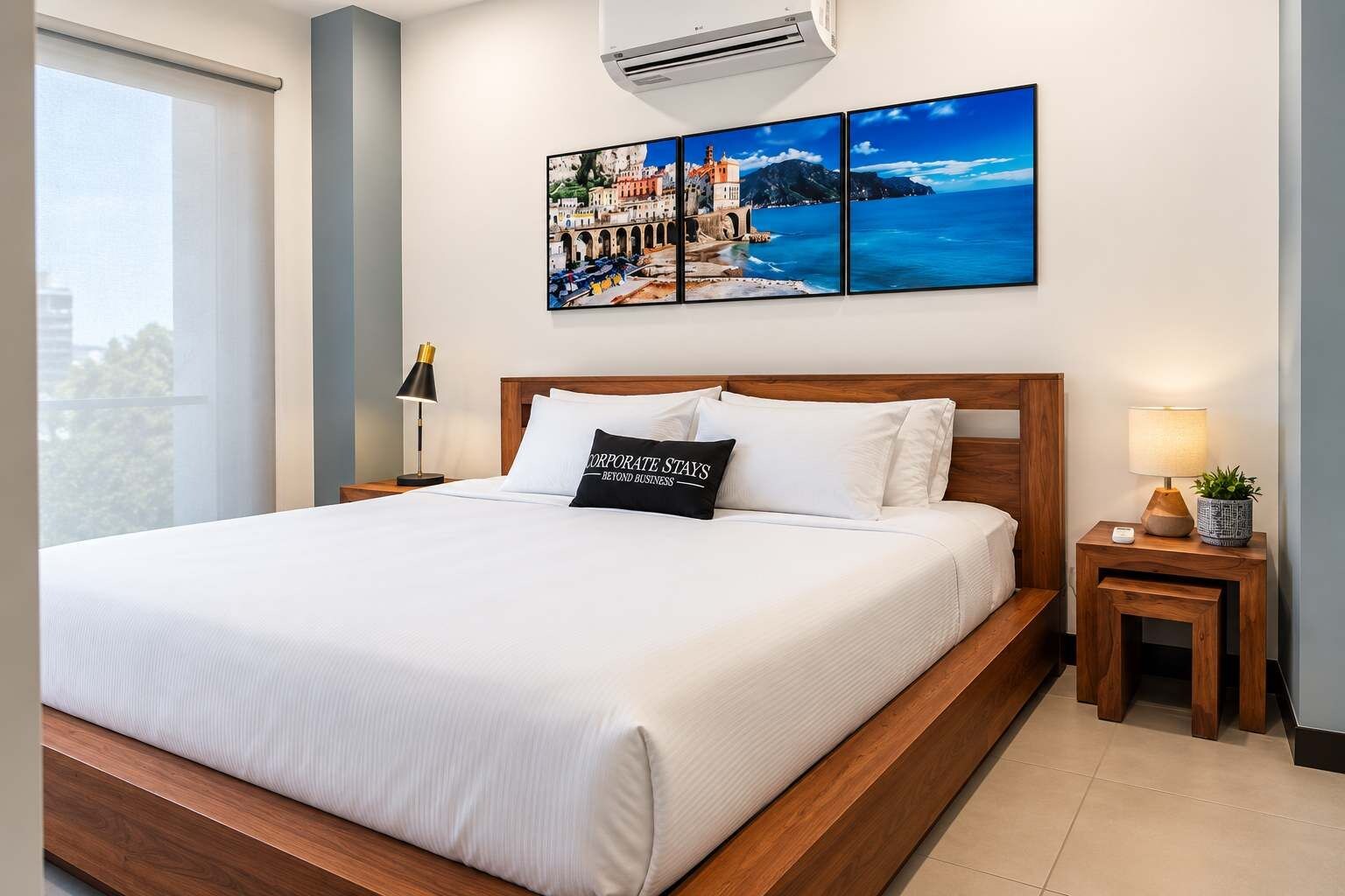 Una habitación de hotel con una cama grande, una mesita de noche con una lámpara, una pequeña mesa con una planta y un aire acondicionado instalado en la pared.