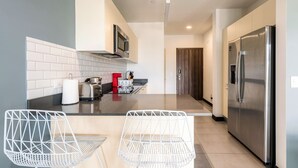 A modern kitchen with a stainless steel refrigerator, a microwave, and a toaster on the countertop. There are two white wire chairs and a small table in the foreground. - Cozy Studio in San José (Pozos)