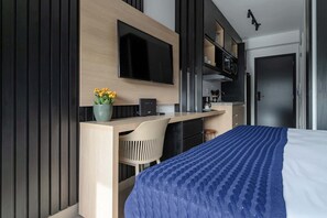 A modern hotel room with a bed, a desk with a chair, a flat-screen TV, a small potted plant, and a kitchenette. - Serviced Studio in São Paulo with City Views (São Paulo)
