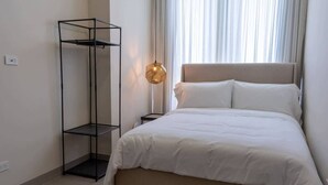 A bedroom with a bed, a tall black metal shelf, a bedside lamp, and a window with curtains. - Furnished Deluxe Condo Suite 2BR with Amazing View (Panamá)