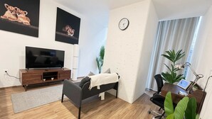 Ett modernt vardagsrum med en platt-TV, en soffa, ett skrivbord med en stol, en klocka på väggen och två stora tavlor.