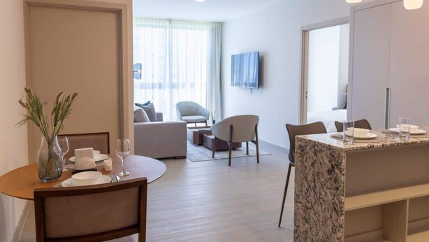 A modern hotel room with a dining area, a sofa, and a TV mounted on the wall. - Modern 2-Bedroom Suite in Panama (Panamá)