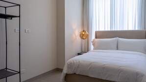 A bedroom with a bed, a hanging light fixture, a wardrobe, and a window with curtains. - Modern 2-Bedroom Suite in Panama (Panamá)