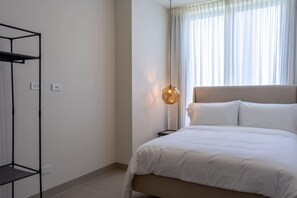 A bedroom with a bed, a hanging light fixture, a wardrobe, and a window with curtains. - Modern 2-Bedroom Suite in Panama (Panamá)
