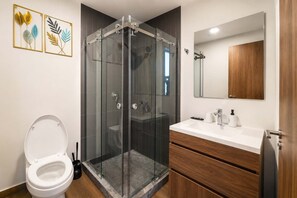 Ein modernes Badezimmer mit einer gläsernen Duschkabine, einer weißen Toilette, einem hölzernen Waschtisch mit Spiegel und einem Bild an der Wand.