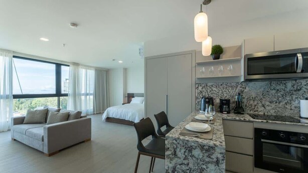 Ein modernes Hotelzimmer mit einem großen Bett, einer Couch, einem Essbereich mit Marmorplatte und einer Küche mit Mikrowelle und Backofen.