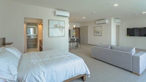 Ein modernes Hotelzimmer mit einem großen Bett, einer Couch, einem Essbereich und einem an der Wand befestigten Fernseher.