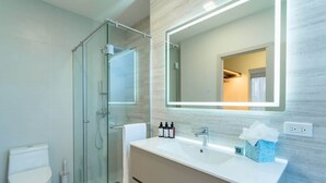 Ein modernes Badezimmer mit Duschkabine aus Glas, einem weißen Waschbecken mit Spiegel und Toilettenartikeln auf der Ablagefläche.