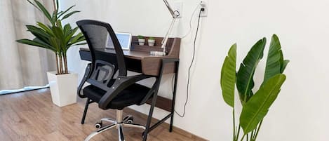 Un espacio de oficina moderno con un escritorio, una silla, una computadora y dos plantas en macetas.