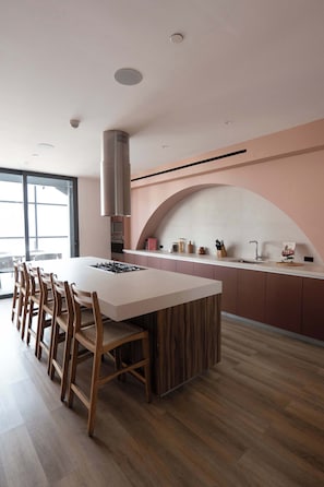 A modern kitchen with a central island, wooden chairs, a stainless steel range hood, and a large window. - Serviced Studio in Mexico City (Mexico City)