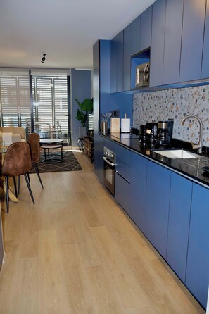 A modern kitchen with blue cabinets, a black countertop, and a coffee maker.