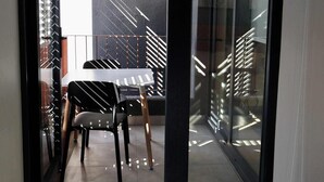 Een moderne slaapkamer met een grote schuifpui die uitkomt op een balkon met een eettafel en stoelen.