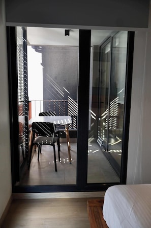 A modern bedroom with a large sliding glass door leading to a balcony with a dining table and chairs. - Furnished 2 Bedroom in Santiago in Greystar Somma (Santiago)