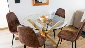 Een ronde glazen tafel met een geweven placemat, omringd door vier beklede stoelen met zwarte poten.