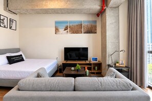 Ein modernes Hotelzimmer mit Bett, Sofa, Fernseher und Kunstwerk an der Wand.