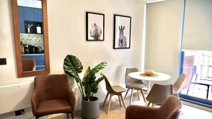 A modern living room with a brown leather chair, a round coffee table, a potted plant, and a dining area with a white table and chairs.