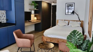 A modern bedroom with a wooden bed, a small round table, a chair, and a desk with a plant.