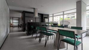 A modern kitchen with a large island, green upholstered chairs, and a view of the city through large windows. - Furnished Studio in São Paulo with City Views (São Paulo)